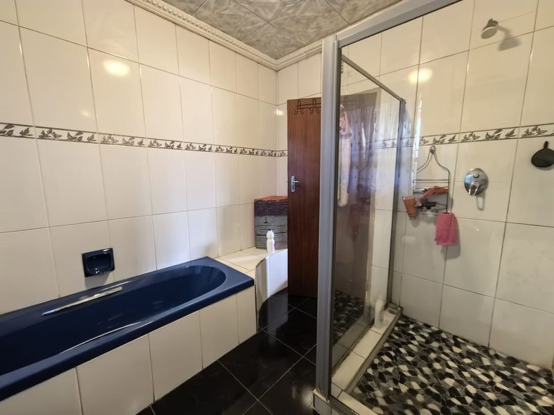 A functional bathroom featuring a built-in blue bathtub, a separate glass-enclosed shower, and tiled finishes throughout.