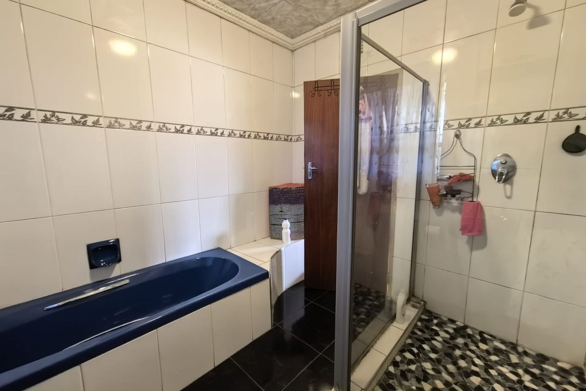 A functional bathroom featuring a built-in blue bathtub, a separate glass-enclosed shower, and tiled finishes throughout.