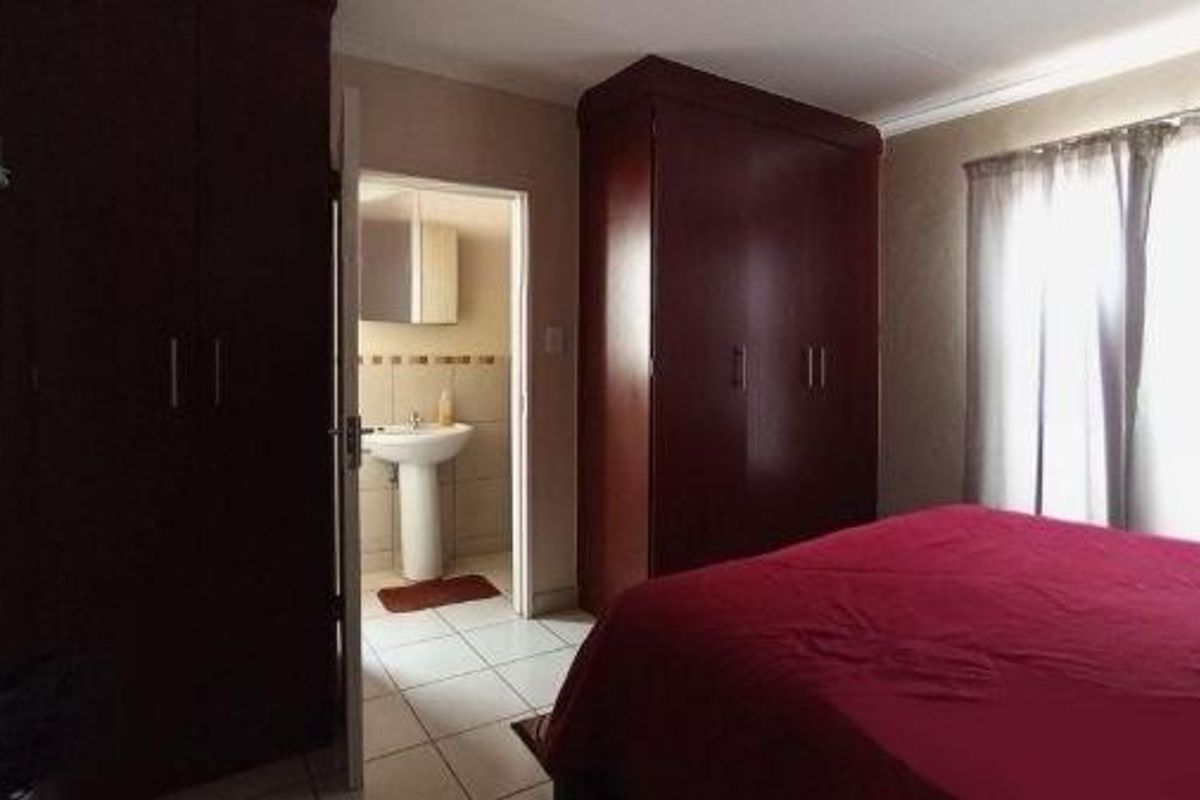 A bedroom featuring built-in dark wood wardrobes and an adjoining en-suite bathroom with a pedestal sink.