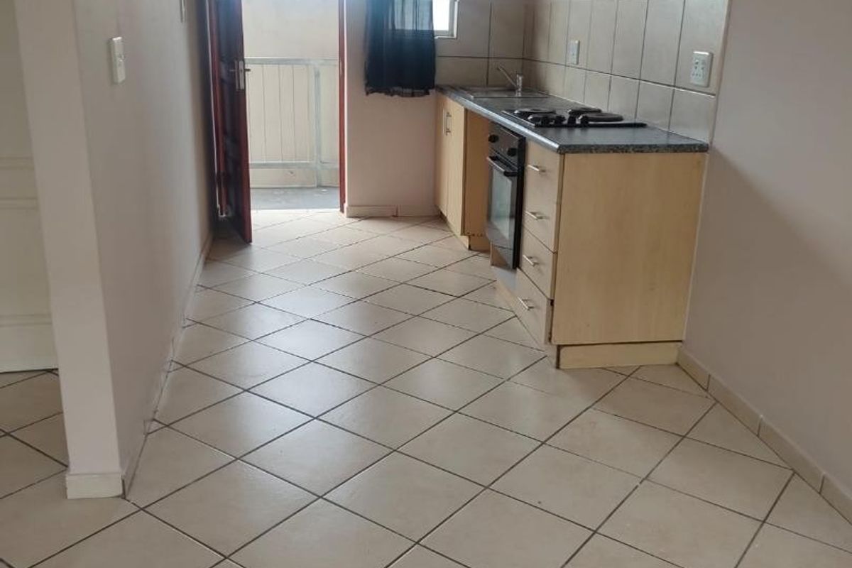 A compact kitchen featuring built-in cabinetry, a hob, an oven, and tiled flooring, with direct access to an outdoor balcony area.