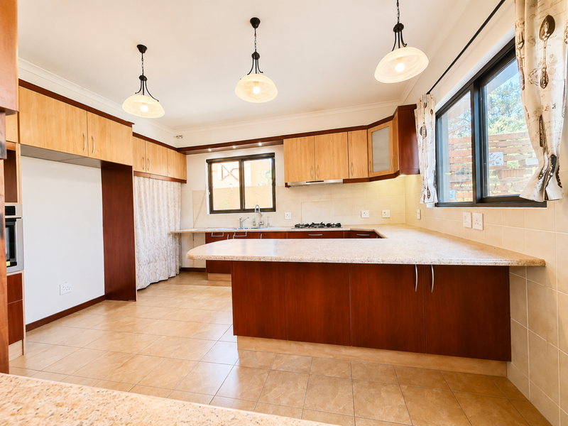 Spacious kitchen featuring warm-toned cabinetry, granite countertops, built-in oven, gas hob, and tiled flooring, offering a functional layout with ample storage space.