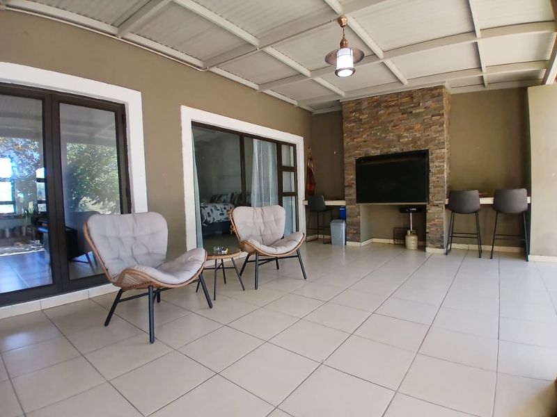 A spacious covered patio featuring tiled flooring, a built-in braai with stone cladding, and direct access to the interior through sliding glass doors.