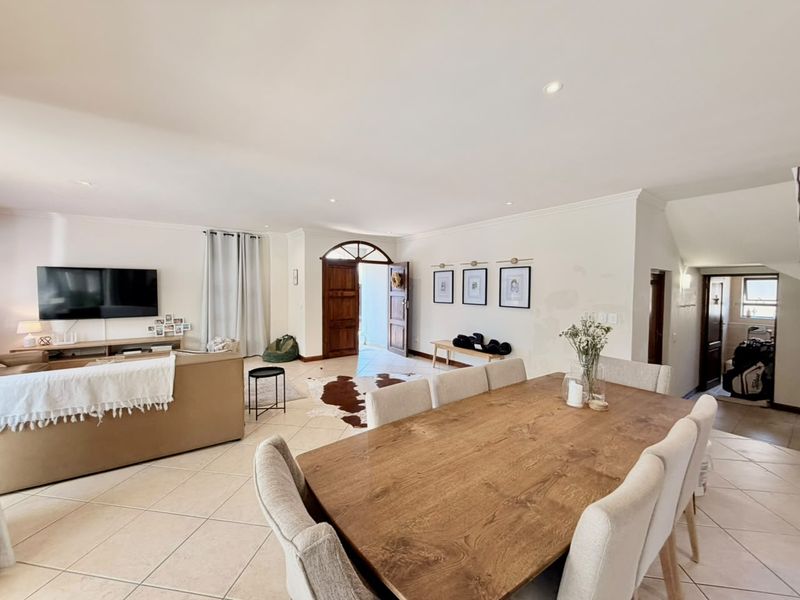 Spacious open-plan living and dining area featuring neutral tiled flooring, recessed lighting, and a distinctive arched wooden entrance door.