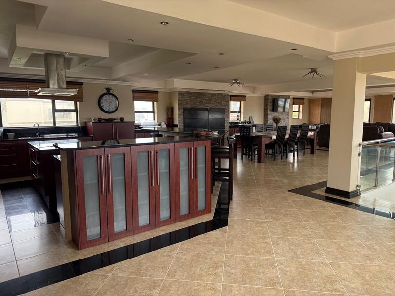 Spacious open-plan living area featuring a modern kitchen with a large island, stone feature wall, and high-quality tiled flooring throughout.