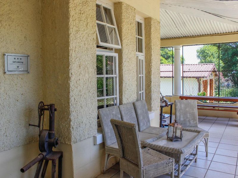 A covered patio area featuring tiled flooring, textured exterior walls, and security mesh fencing, providing a functional outdoor space for the guest house.