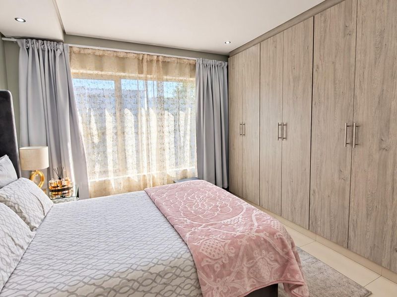 A well-maintained bedroom featuring extensive built-in cupboards, neutral tiled flooring, and recessed downlighting, creating a clean and functional living space.