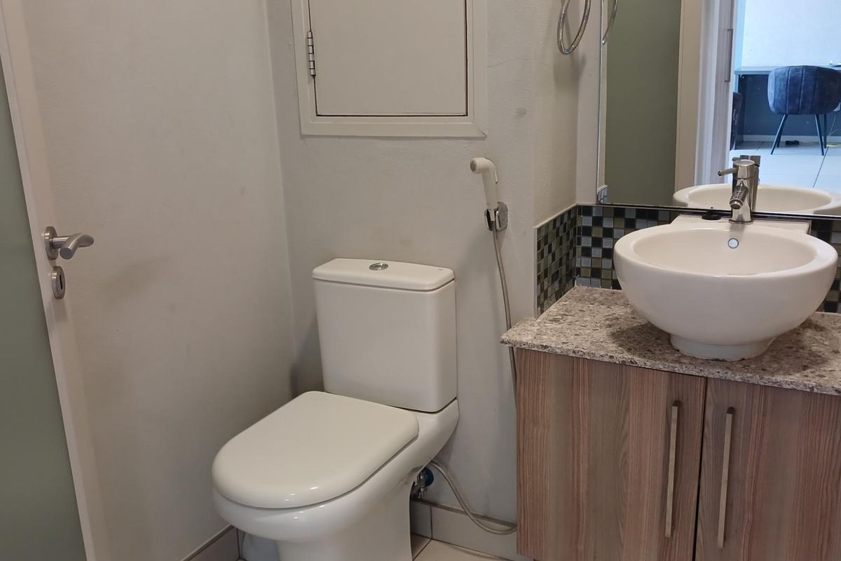 A compact bathroom featuring a modern vessel sink on a stone-topped vanity, a dual-flush toilet, and a bidet spray attachment.