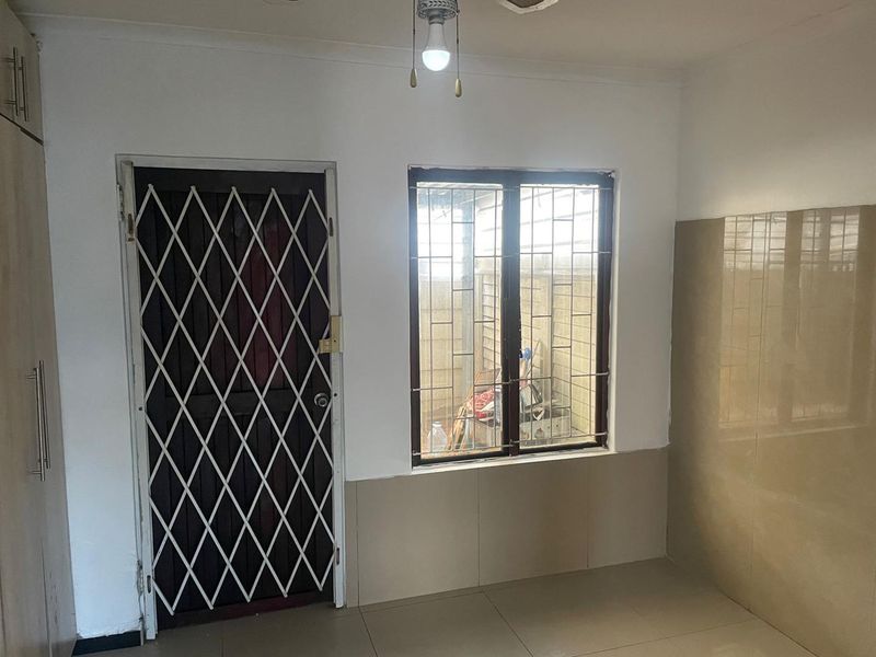 A functional kitchen area featuring tiled flooring, built-in cabinetry, and a security gate leading to the exterior.