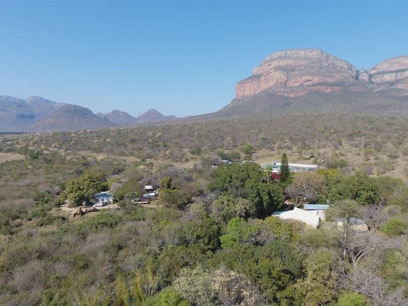 An aerial view of the farm property, showcasing the main homestead, various outbuildings, and surrounding natural landscape with mountain vistas.