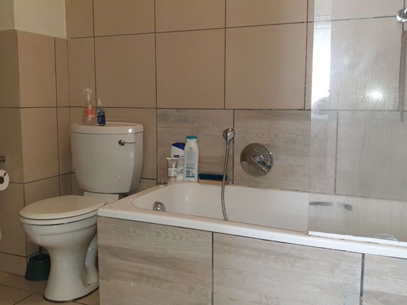 A functional bathroom featuring a bathtub with a glass shower screen, tiled walls, and standard sanitary fixtures.