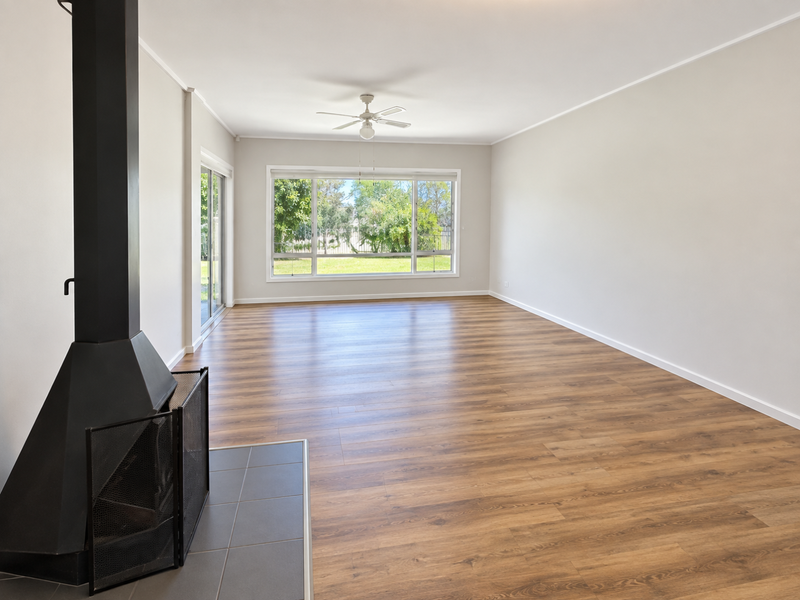 Spacious, light-filled living room featuring modern laminate flooring, a striking freestanding fireplace with a tiled hearth, and large windows overlooking the garden.