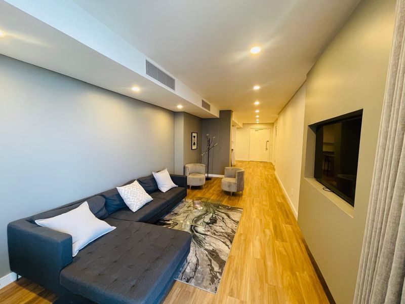Modern living room featuring timber laminate flooring, recessed downlights, ducted air conditioning, and a built-in television wall niche.
