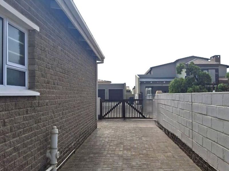 A side passage featuring brick paving, a cinder block boundary wall, and a timber gate leading to the rear of the property.