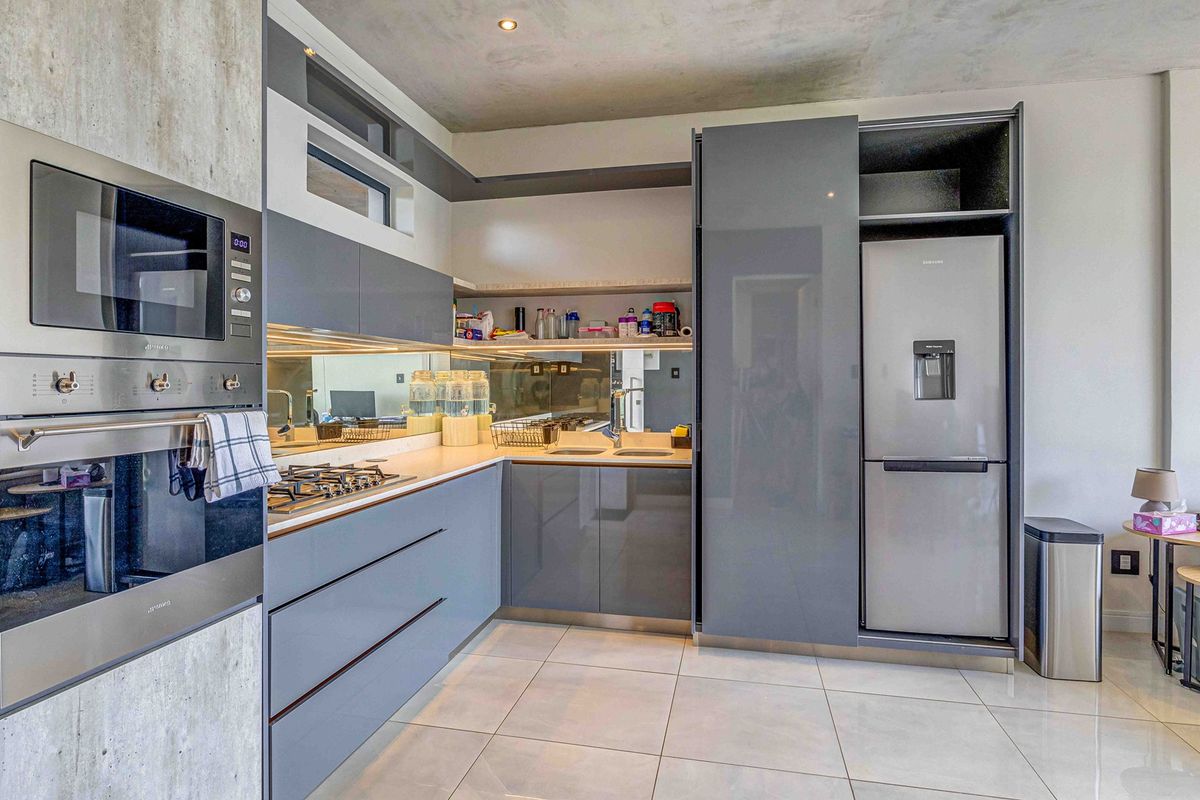 Modern kitchen featuring high-gloss grey cabinetry, integrated appliances, gas hob, built-in oven, microwave, and a sleek mirror splashback with tiled flooring.