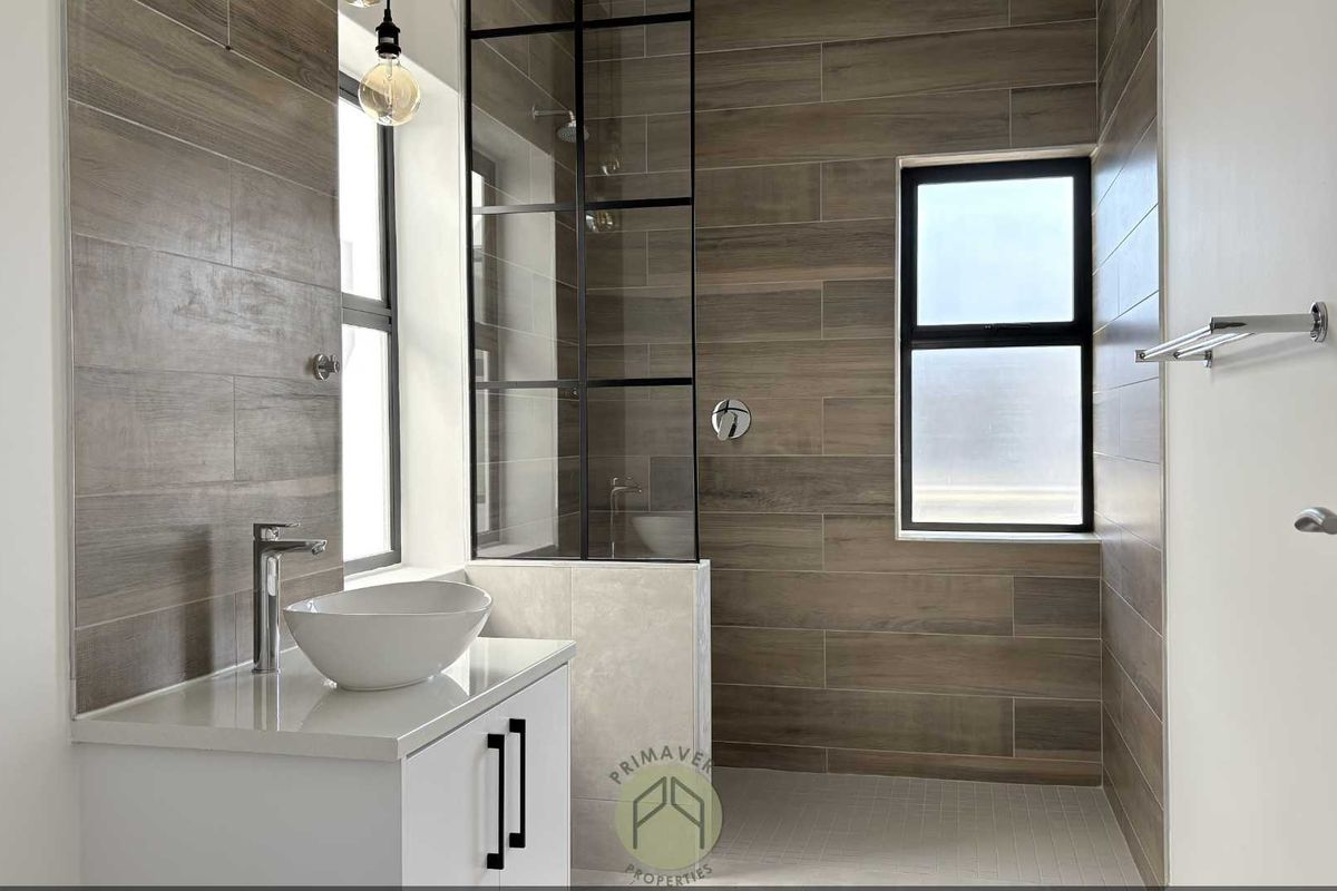 Modern bathroom featuring wood-look wall tiles, a glass-enclosed walk-in shower, a contemporary vanity with a vessel sink, and black-framed window fixtures.