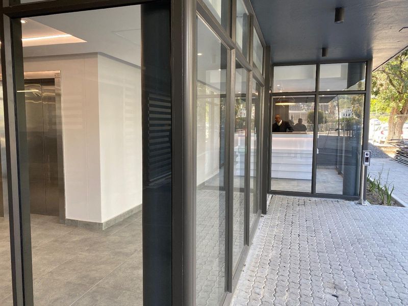 Modern apartment building entrance featuring a glass facade, tiled walkway, and stainless steel elevator access.