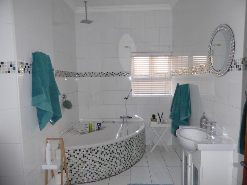 A bright bathroom featuring a corner bathtub with mosaic tiling, a vanity basin, and a combination overhead and handheld shower system.