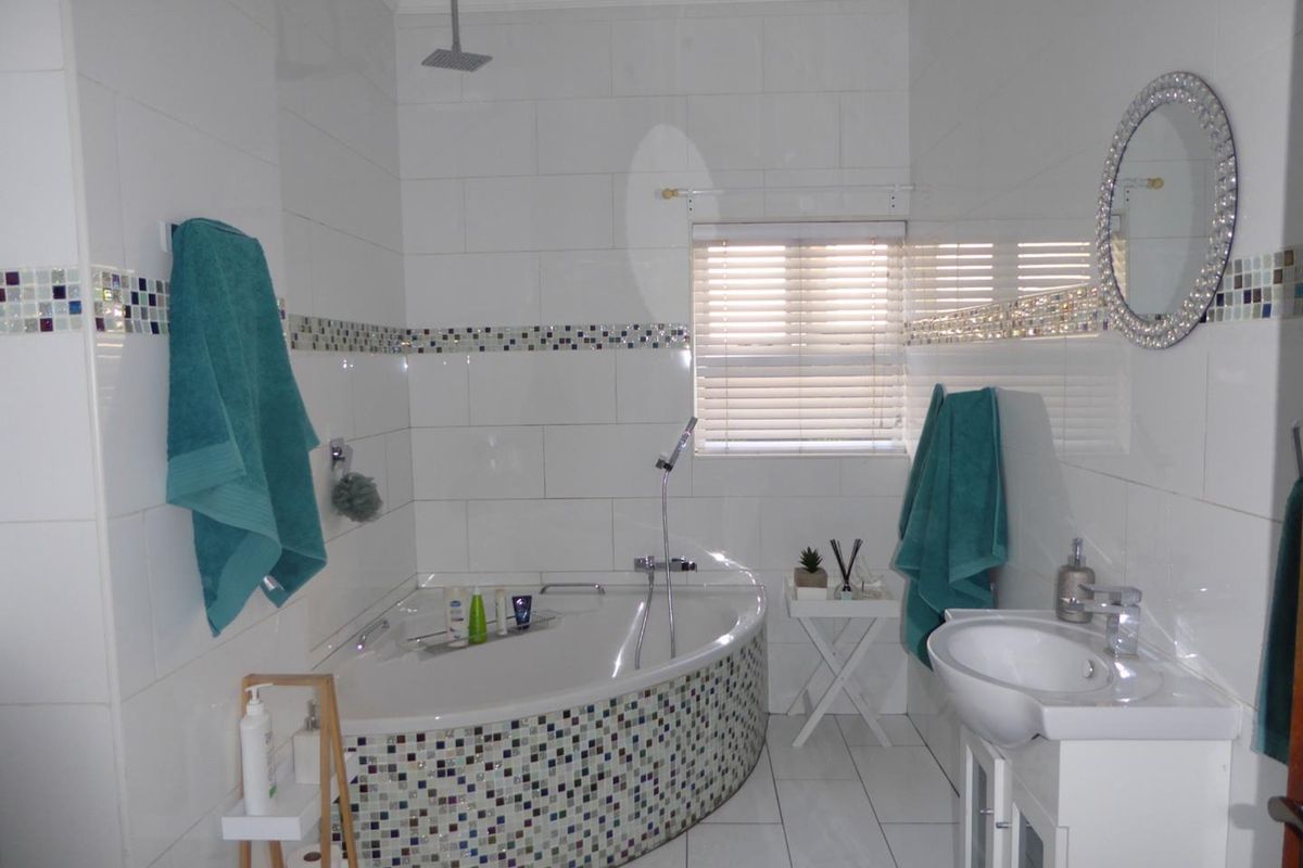 A bright bathroom featuring a corner bathtub with mosaic tiling, a vanity basin, and a combination overhead and handheld shower system.