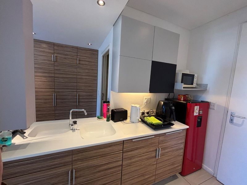 Compact kitchen featuring modern wood-grain cabinetry, white countertops, an integrated sink, and recessed ceiling lighting.