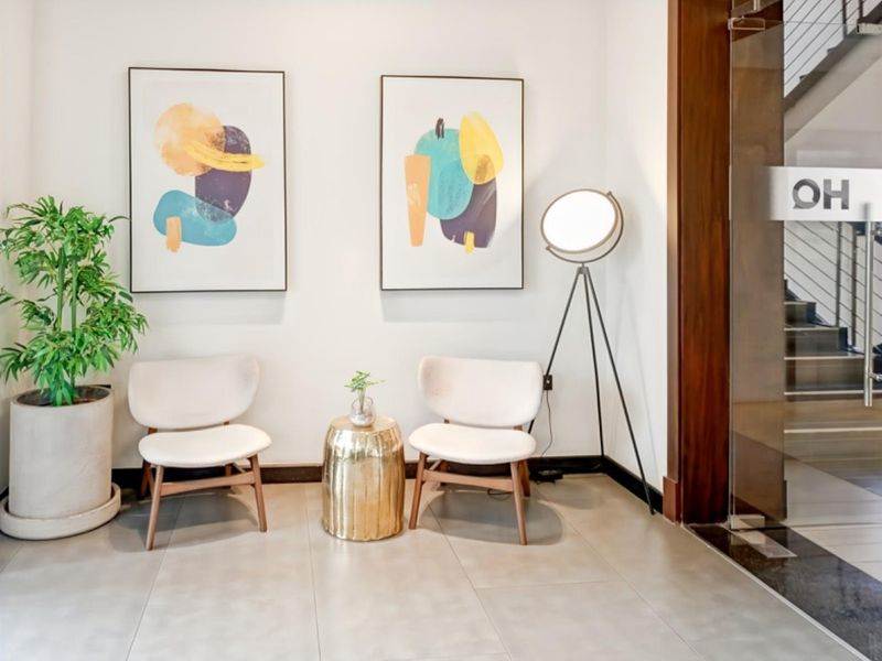 A bright and modern office entrance area featuring clean tiled flooring and a glass door with wooden framing.