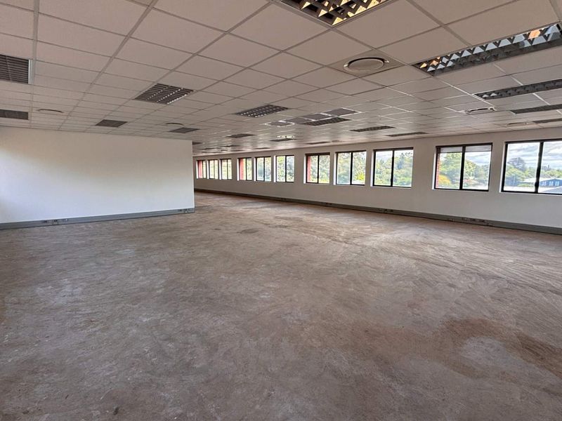 A spacious, open-plan office area featuring a suspended ceiling, recessed lighting, and extensive windows providing ample natural light.