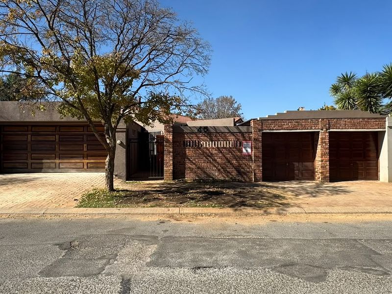 Front elevation of the property featuring a brick facade, three garage doors, and a paved driveway with secure gated access.