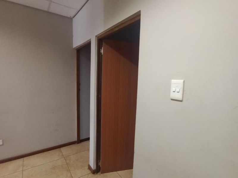 A functional office hallway featuring tiled flooring, suspended ceiling tiles, and timber door frames leading to adjacent rooms.