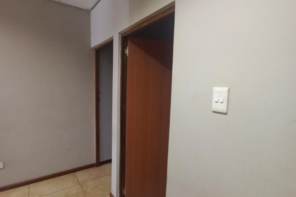 A functional office hallway featuring tiled flooring, suspended ceiling tiles, and timber door frames leading to adjacent rooms.