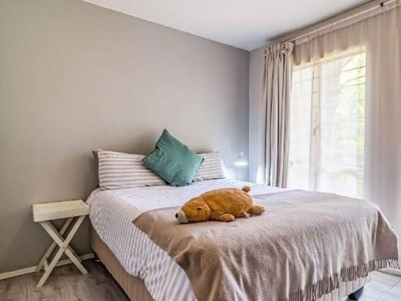 A well-lit bedroom featuring neutral wall tones, laminate flooring, and built-in cupboards with modern hardware.