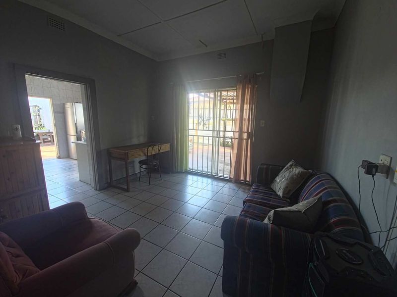 A living room featuring tiled flooring and a sliding glass door with security gate, providing access to the exterior.