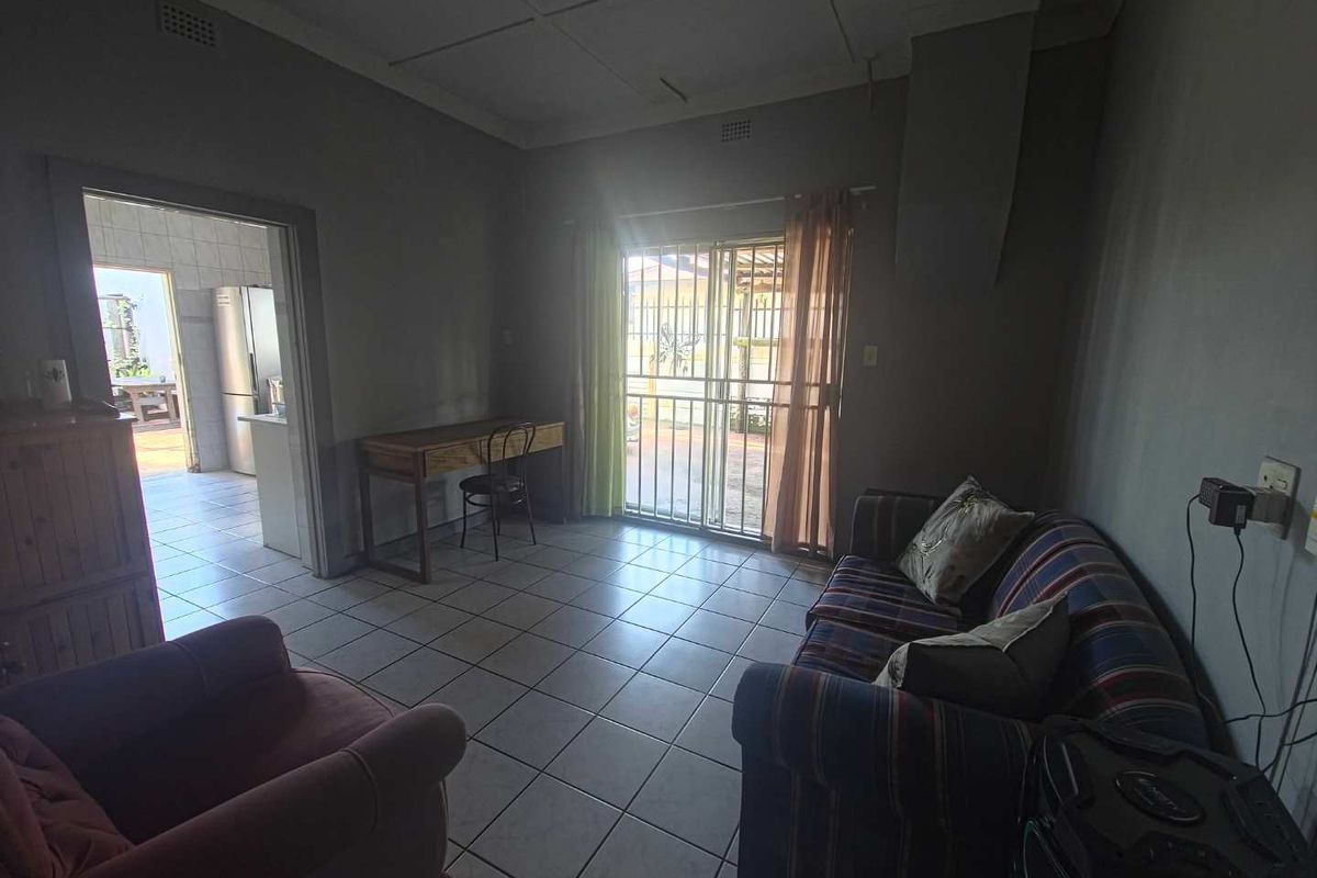 A living room featuring tiled flooring and a sliding glass door with security gate, providing access to the exterior.