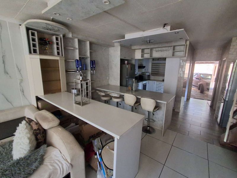 Open plan living area featuring a built-in bar and kitchen with stone countertops, tiled flooring, and recessed lighting, requiring some cosmetic updates.