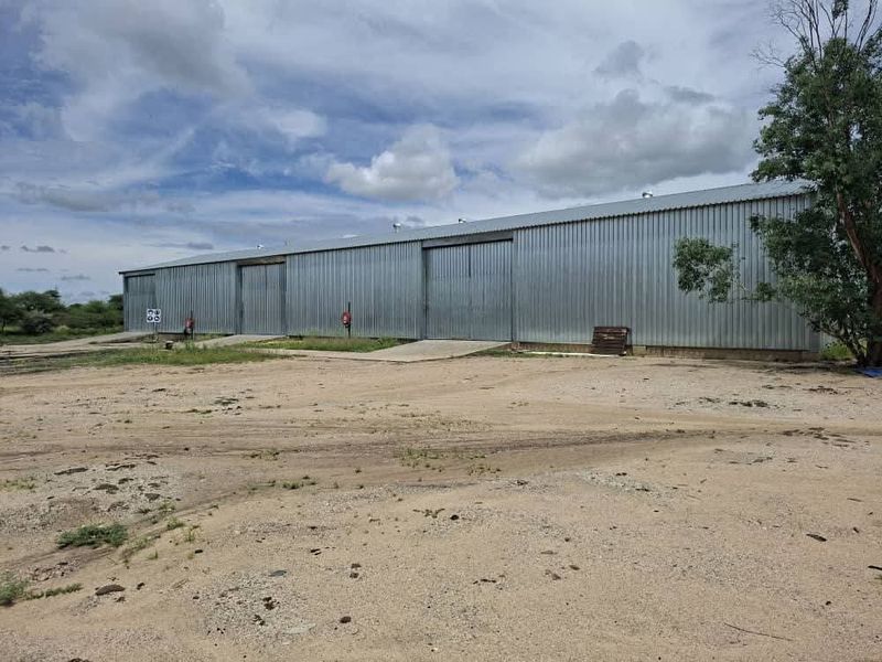Industrial warehouse building featuring corrugated metal cladding, multiple sliding access doors, and concrete loading ramps on a large unpaved site.