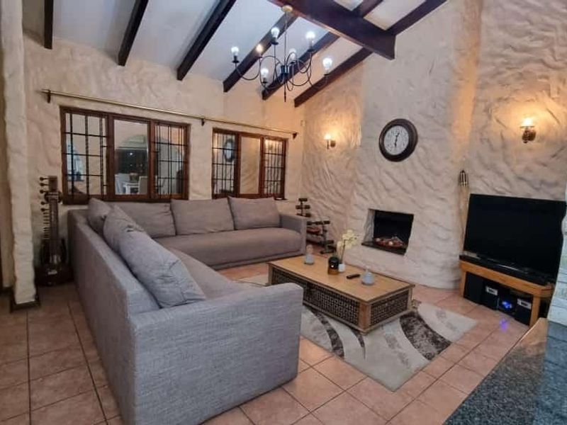 Cozy living room featuring exposed timber ceiling beams, textured plaster walls, tiled flooring, and a built-in fireplace.