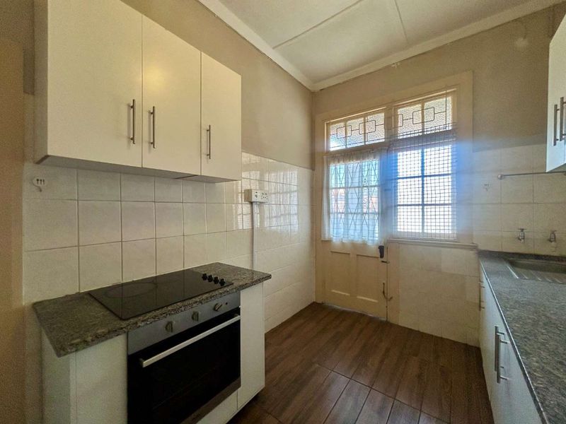 A functional kitchen featuring built-in cabinetry, granite countertops, an electric hob, and an oven, with direct access to an exterior door.