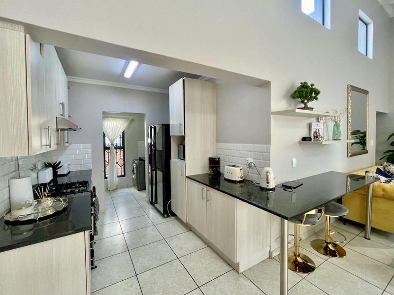 Modern open-plan kitchen featuring light wood cabinetry, granite countertops, a breakfast bar, and a subway tile backsplash, seamlessly flowing into the living area.