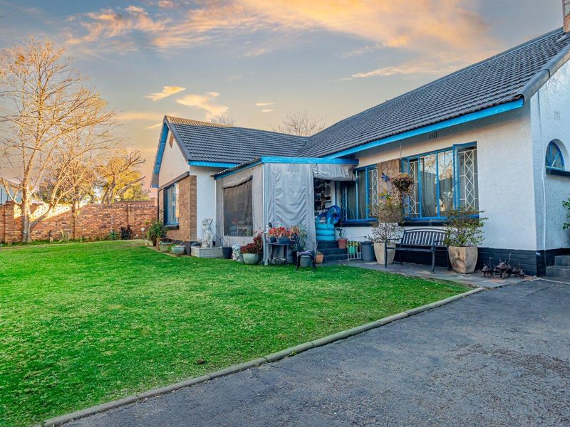Rear view of the house featuring a lawn, paved driveway, covered patio area, and stone cladding accents on the exterior walls.