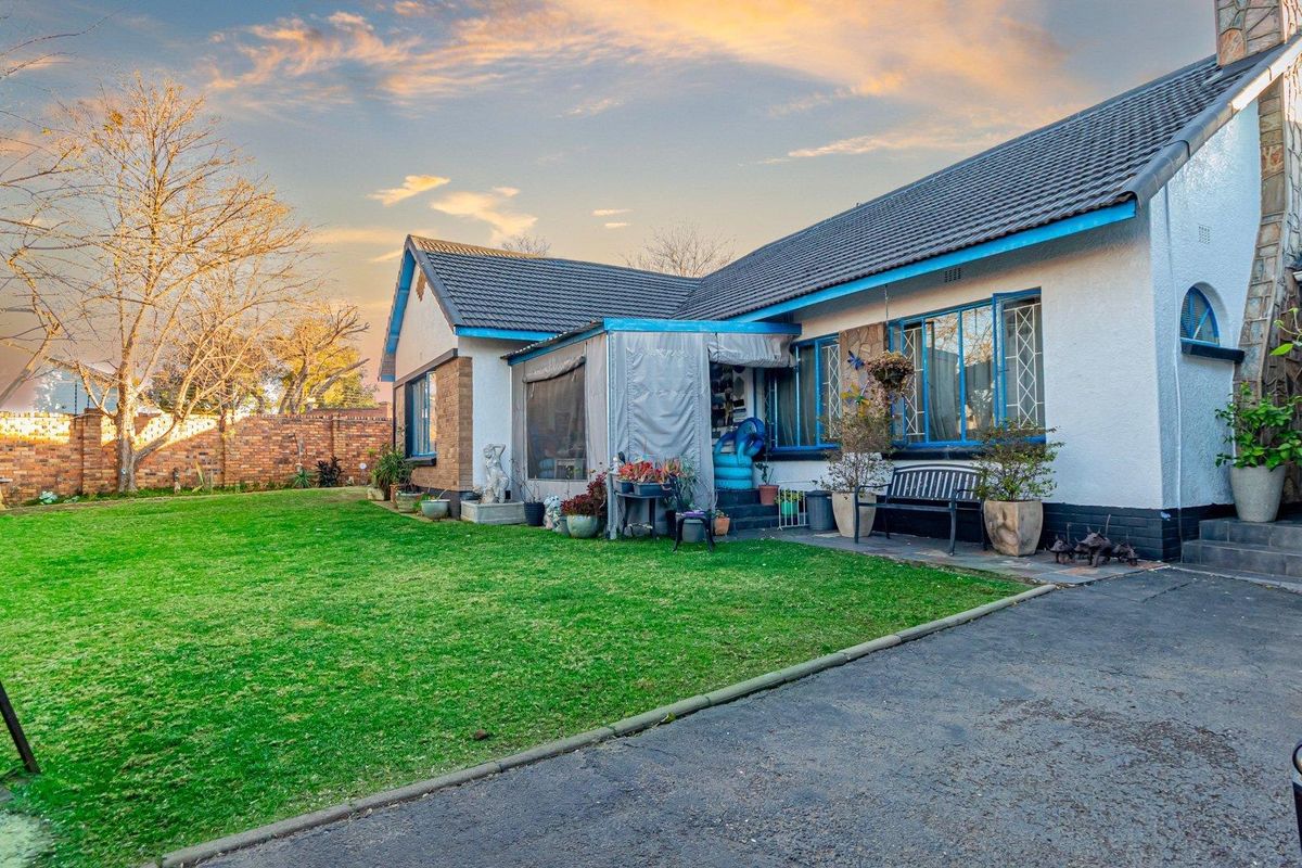 Rear view of the house featuring a lawn, paved driveway, covered patio area, and stone cladding accents on the exterior walls.