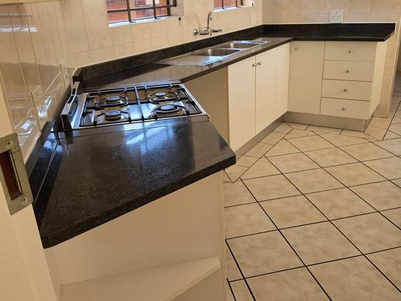 A clean, functional kitchen featuring white cabinetry, dark countertops, a gas hob, and tiled flooring with a neutral backsplash.