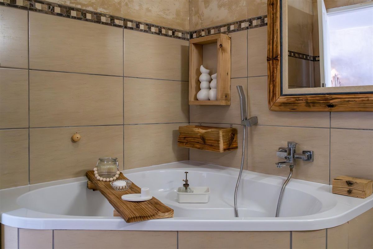 A corner bathtub featuring beige wall tiling with a decorative mosaic border and wall-mounted chrome faucet fixtures.