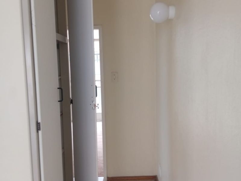A functional hallway featuring tiled flooring, a built-in storage cupboard, and a wall-mounted light fixture, providing access to adjacent living areas.