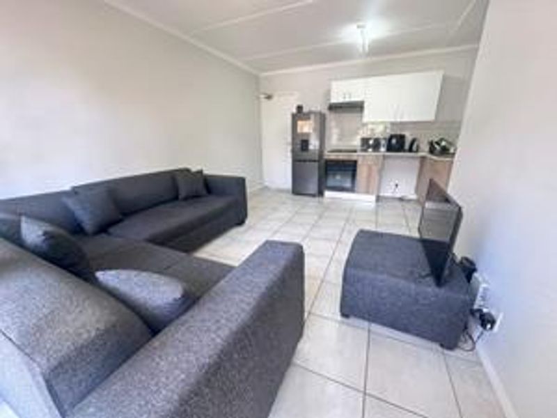 Open-plan living area featuring tiled flooring and a functional kitchen with built-in cabinetry, oven, and hob.