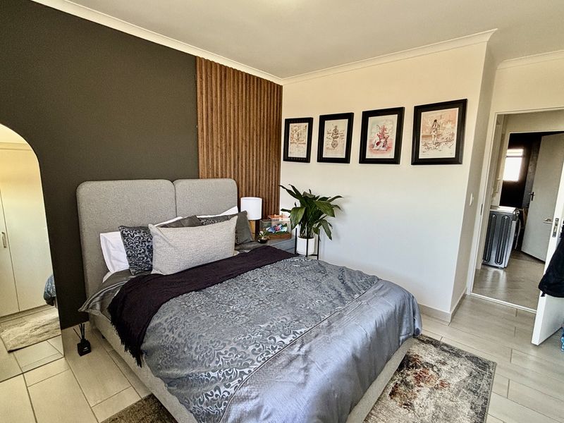 A well-maintained bedroom featuring tiled flooring, a modern accent wall with timber-look paneling, and a built-in wardrobe.