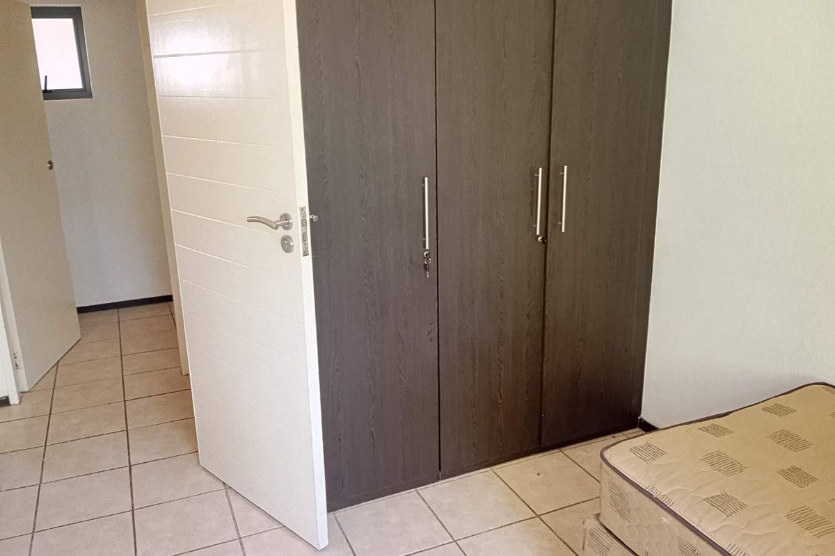 A bedroom featuring tiled flooring and a dark wood-finish built-in wardrobe with modern handles.