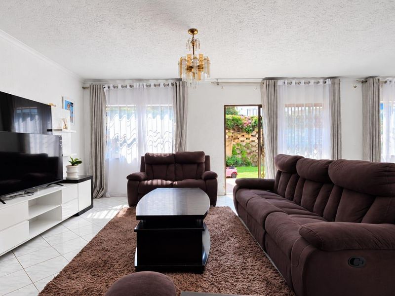Spacious living room featuring tiled flooring, a central chandelier, and direct access to the rear garden through a sliding glass door.