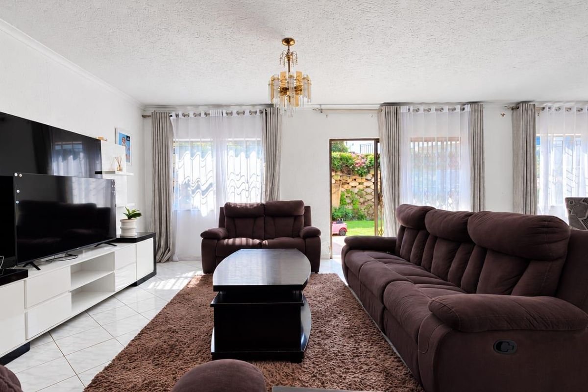Spacious living room featuring tiled flooring, a central chandelier, and direct access to the rear garden through a sliding glass door.