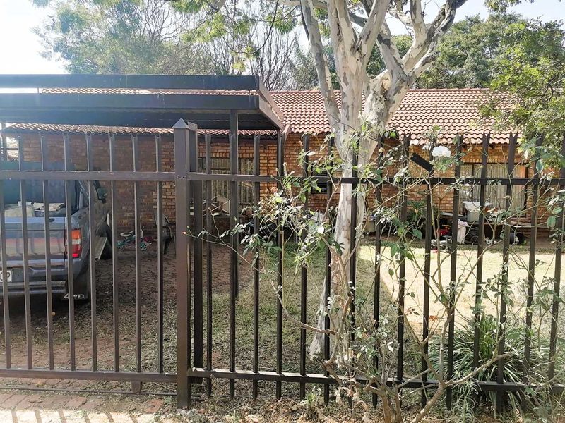 Front view of a brick house featuring a metal carport and secure perimeter fencing.