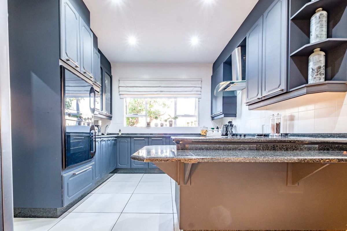 Modern kitchen featuring dark blue cabinetry, granite countertops, a breakfast bar, built-in oven, and extractor fan with tiled flooring.