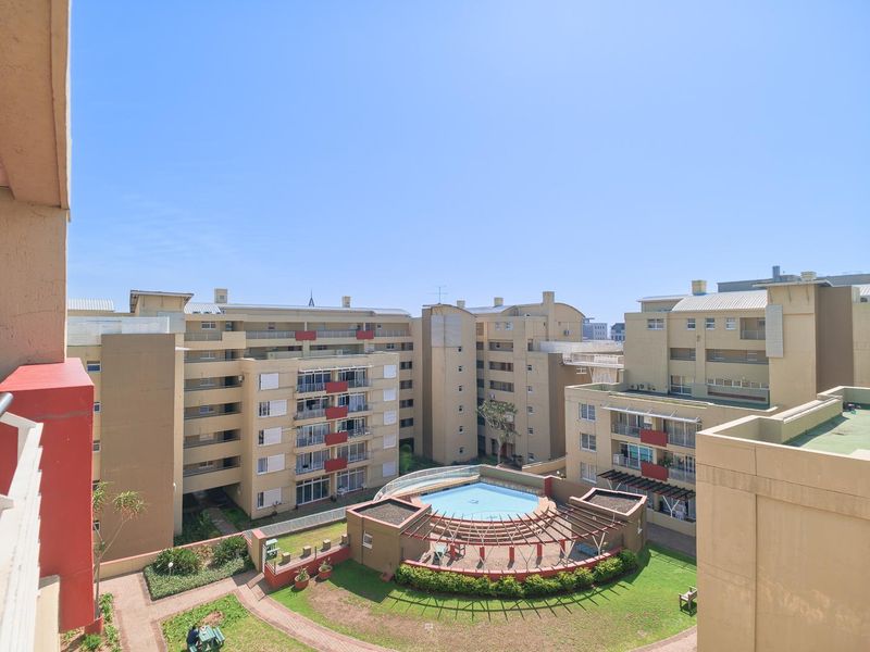 Elevated view overlooking the complex communal swimming pool, landscaped gardens, and surrounding residential townhouse blocks.