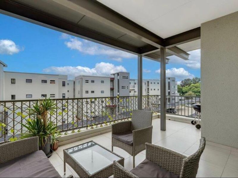 A spacious covered balcony featuring tiled flooring and a secure metal balustrade, offering an open-air outdoor living space.